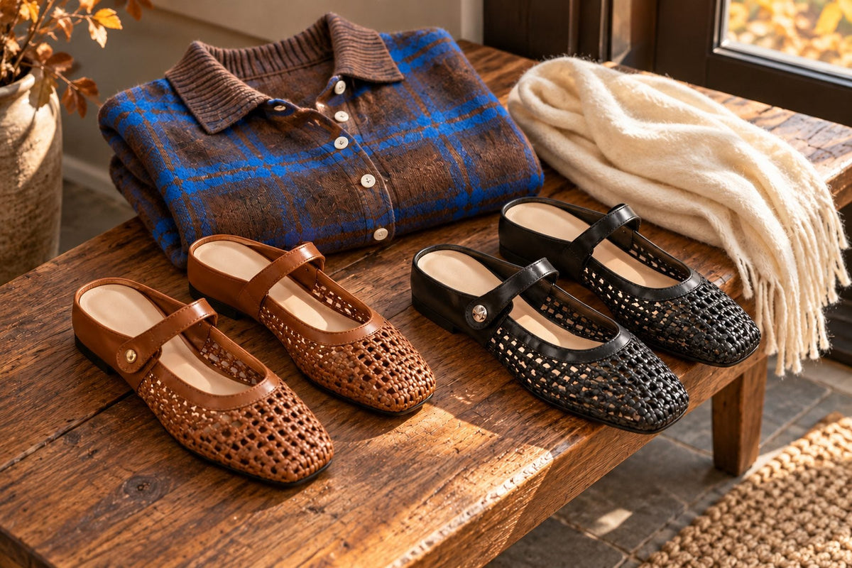 Brown and black woven Mary Jane flats on a wooden entry bench beside a folded brown plaid knit cardigan in fall light