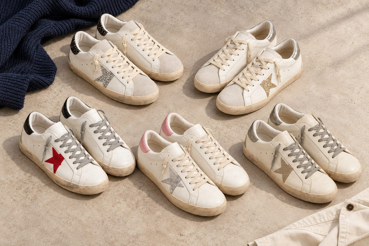 Five pairs of men's white leather sneakers with colored star patches and worn-in soles laid out on pale concrete